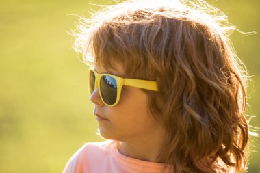 Lifestyle portrait of cute kid outdoors. Summer kids outdoor portrait. Close-up face child playing outdoors in summer park. Kid having fun outdoor on sunny summer day