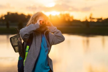 Çocuk keşif konsepti. Dürbünle oynayan mutlu çocuk. Keşif ve macera. Sırt çantalı çocuk doğayı ve çevreyi keşfediyor. Çocuklar için açık hava eğlence etkinliği