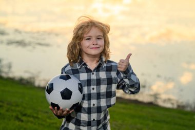 Çocuk çocuk klasik futbol topunu parkta tutuyor. Çocuk futbol topu, afiş. Futbol topu olan çocuk. Spor, çocuklar için futbol hobisi. Futbol topuyla poz veren küçük bir futbolcu