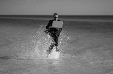 Heyecanlı yaz seyahati. Serbest çalışma, online çalışma. Takım elbiseli yaz işadamı deniz suyunda koşuyor. Serbest seyahat demek. Takım elbiseli komik serbest çalışan atlayıp denizde koşuyor. Serbest çalışmak ve tatiller