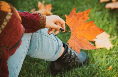 Mevsimsel konsept. Sarı akçaağaç yaprağı parkta bir kadının elini tutuyor. Üstten yakından bak. Mevsimsel konsept. Sarı sonbahar iznini tutan kadın. Sarı meşe yaprağını tutan kadın.