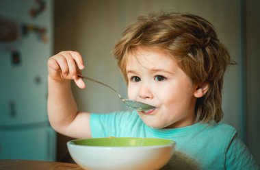 Şirin çocuk bebek çocuk Mama sandalyesinde oturan ve bulanık arka planda yeme gülüyor. Neşeli bebek çocuk kaşık ile yiyecek kendisi yiyor. Ebeveyn -lik. Masada oturan ve süt atıştırmalıkları yiyen küçük çocuk.
