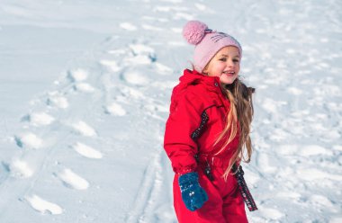Çocuk kışın karla oynuyor. Noel 'de kış parkında örgü şapkalı küçük bir kız. Çocuklar karlı ormanda oynayıp zıplıyorlar.