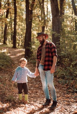 Babam kovboy. Aile zamanı. Aile eğlencesi. Doğayı keşfet. Seyahat tutkusu konsepti. Vahşi sakallı adam ve küçük çocuk ailesi doğanın tadını çıkarıyor. Hippi sakallı baba ve tatlı oğlu ormanda birlikte vakit geçiriyorlar..