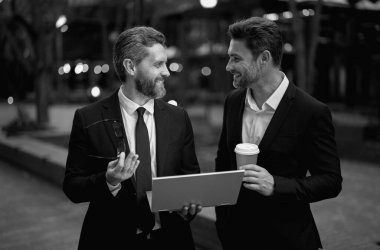 İki iş ekibinin paket kahve ve dizüstü bilgisayarla dışarıda buluşmasını planlıyorum. İş adamları dışarıda dizüstü bilgisayar kullanıyor. İş adamları şehir planındaki iş başarılarıyla dizüstü bilgisayarı arıyorlar.