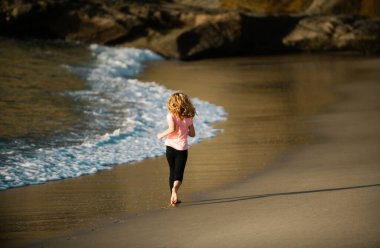 Deniz sahilinde koşan mutlu çocuk. Komik çocuk sörf kenarına doğru koşuyor. Aktif çocuk yaşam tarzı. Eğitimdeki küçük bir atlet. Koşucu spor yapıyor, çocuklar için koşuyor.