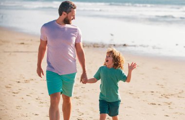 Baba ve oğul denizde yürüyor. Baba ve çocuk dışarıda oynuyorlar. Arkadaş canlısı aile kavramı ve yaz tatili