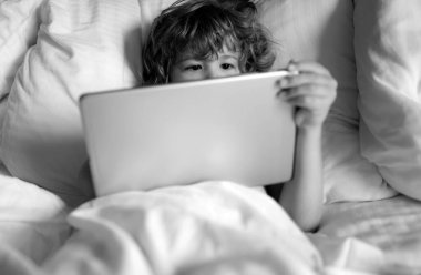 Sosyal ve teknoloji konsepti. Çocuklar internet. Yatakta tabletli çocuk. Ebeveyn izni, güvenlik ağı. Çocuk çevrimiçi oyun oynuyor