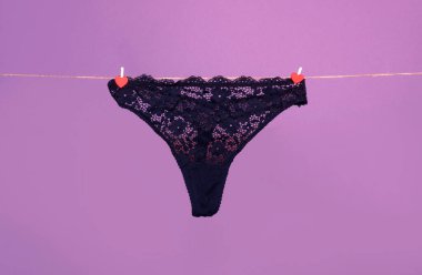 Panties. Female lace lingerie. Womans erotic black underwear panties. Womens panties hanging on rope isolated on purple background