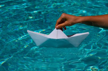 Paper boat sailing on water causing waves and ripples. Tourism and traveling, travel dreams vacation holiday, sailing adventure. Hand putting a paper boat into water