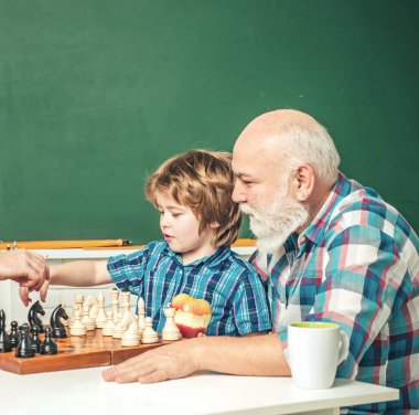 Grandfather and grandson playing chess. Grandpa teaching grangson at chess school