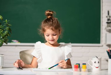 Boyama kalemleriyle resim çizen çocuk. Okulda sanat ve zanaat dersinin tadını çıkarırken mutlu bir şekilde gülümseyen küçük kızın portresi. Çocukluk eğitimi, çocukların sanatsal becerileri.