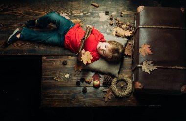 Küçük şirin çocuk sonbahar yaprakları ile bir ahşap zemin üzerinde yatıyor ve kitap okumak. Sonbaharda oynayan çocuk. Çocuklar için bütün sonbahar kıyafetleri için en büyük indirimler