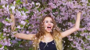 Dışarıda gül yapraklı güzel bir kadın var. Bahar çiçekleri atan mutlu kadın. Bahar titreşimleri. Doğa portresi. Güzel kadının üzerine kiraz yaprakları düşüyor. Sakura çiçekleri atan kız.