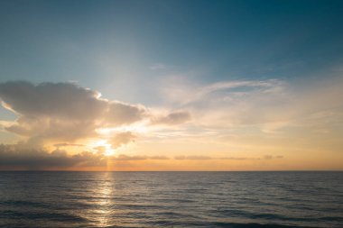 Gökyüzü ve bulutların arasından güneş batarken deniz batıyor. Okyanus ve gökyüzü arkaplanı, deniz manzarası.