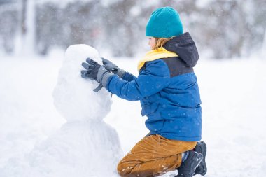 Mutlu Çocuk kışın kardan adam için kartopu yapıyor. Çocuk karda oynuyor. Açık havada aktif kış oyunları. Çocuk karla oynarken eğleniyor. Çocuklar için açık havada kış tatili. Güneşli kış gününde çocuk oyunu