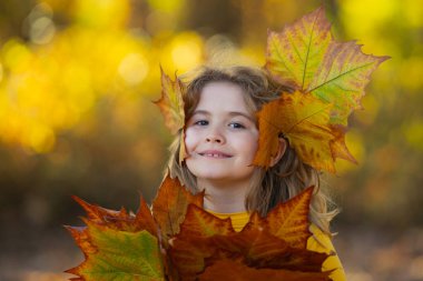 Akçaağaç yapraklı çocuklar arka planda. Sonbahara yakın bir çocuk güneş ışığında yapraklarını döküyor. Sonbahar sonbahar parkında küçük bir çocuk. Çocuklar ve yapraklar, dökülen yapraklar. Sonbahar yaprağı. Düşen yapraklar