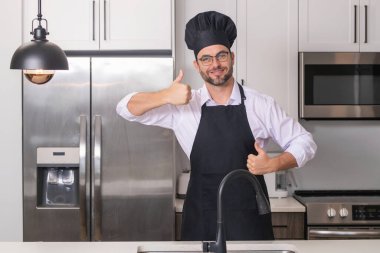 Mutlu fırıncı, baş parmak yukarıda. Aşçı, aşçı ya da fırıncı portresi. Aşçı şapkalı ve aşçı üniformalı adam mutfakta yemek pişiriyor.