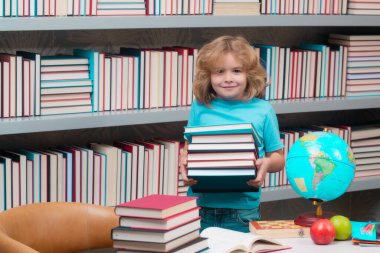 Kütüphanede yığınla kitabı olan okul çocuğu. Okul çocukları. İlkokuldan bir çocuk. Öğrenci, git çalış. Zeki okul çocuğu öğreniyor. Çocuklar eğitim, bilgi ve eğitim kavramı