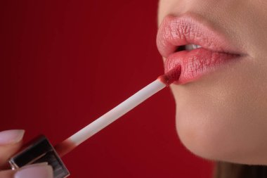 Seksi dudaklarıma ruj sürüyorum. Parlak rujla boyanmış dudaklar, yakın plan. Şımartma, dudak düzeltme konsepti. Dolgun, şehvetli dudağında parlak bir ruj. Ruj süren kadın eli