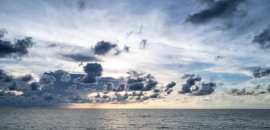 Denizde gün batımı. Sakin bulutlu gökyüzü ile okyanus sahili gündoğumu