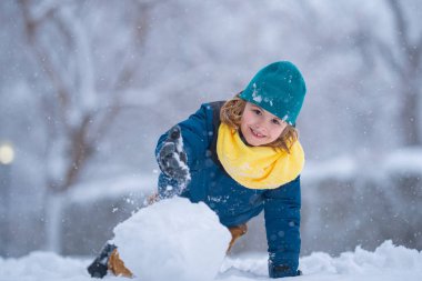 Mutlu Çocuk kışın kardan adam için kartopu yapıyor. Çocuk karda oynuyor. Açık havada aktif kış oyunları. Çocuk karla oynarken eğleniyor. Çocuklar için açık havada kış tatili. Güneşli kış gününde çocuk oyunu