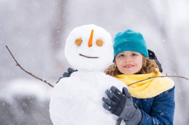 Soğuk bir kış gününde, kış parkında mutlu çocuk. Kışın karla oynayan sevimli bir çocuk. Kardan adamla komik çocuk portresi. Noel 'de kış aktiviteleri. Parkta kardan adam yapan çocuk