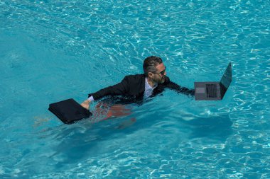 İş adamı dışarıda yüzme havuzunda dizüstü bilgisayardan izliyor. Havuz suyunda dizüstü bilgisayar kullanan mutlu orta yaşlı iş adamı yönetici CEO 'su. Yaz havuzunda bilgisayar başında çalışan serbest çalışan işadamı