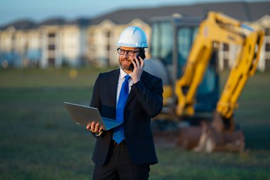 İnşaat mühendisi ya da inşaat mühendisi. İnşaat alanında kask ve takım elbiseli mühendis. Kazıcının yanındaki inşaat müdürü. Yenileme konsepti