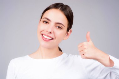 Genç kadının yakın plan portresi, parmak izini gri arka planda gösteriyor. Kadın eli baş parmağını gösteriyor. Başparmak kaldıran bir el. Başparmağı havada Mutlu Kadın
