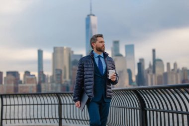 New York 'ta ceketli bir iş adamı kahve içer. Sonbaharda New York, Manhattan 'da iş adamı. Sonbaharda dışarıda yakışıklı bir iş adamı. Ceketli olgun bir adam yürüyor ve içiyor kahveyi götürüyor.