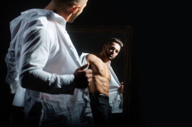 Beyaz gömlekli, seksi, çıplak vücutlu, modacı erkek manken. Siyah arka planda düğmesiz beyaz gömlekli seksi bir adam. Çıplak gövdesi ve gömleği olan yakışıklı kaslı adam. Açık tişörtlü adam.