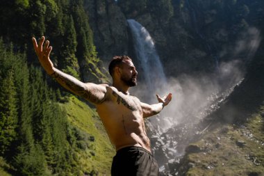 Yaz tatilindeki erkek turist. Yaz tatilinde çıplak gövdeli yakışıklı bir adam. Dışarıda seksi bir yürüyüşçü var. Şelale manzarasında yürüyen bir turist. İnsan Seyahati ve doğa