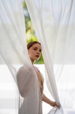 Pencere perdelerinde poz veren lüks dairede romantik bir kadın. Zayıf vücutlu romantik bir kadın. Güzel romantik model. Güzel romantik kadın yüzü. İçerideki güzel kız.