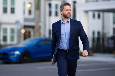 Klasik takım elbiseli, mavi ceketli ve beyaz gömlekli bir iş adamı. Takım elbiseli moda adamı dışarıda yürüyor. Moda elbisesi giymiş bir iş adamı şehirde yürüyor. İş dünyası moda tarzı. Moda kıyafetli bir adam. Modern