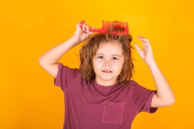 Saç bakımı ve çocukların saç şekillendirmesi. Sarışın, uzun saçlı çocuk saçlarını taramaya çalışıyor. Taraklı bir saç portresi.