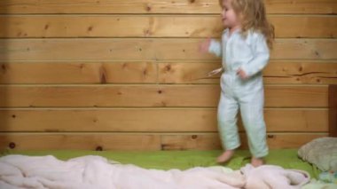Heyecanlı pijamalı bebek gülüyor ve eve yatağa atlıyor. Çocukluk, günaydın. Bebek yatakta zıplıyor, evde eğleniyor. Çocuk zıplayarak ve yatakta oynayarak eğleniyor. Yatak odasında bebek oyunu