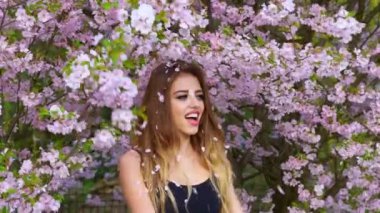 Dışarıda gül yapraklı güzel bir kadın var. Bahar çiçekleri atan mutlu kadın. Bahar titreşimleri. Doğa portresi. Güzel kadının üzerine kiraz yaprakları düşüyor. Sakura çiçekleri atan kız.