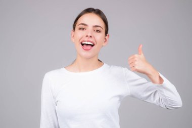 Gri arka planda izole edilmiş genç kız baş parmağını gösterdi. Kadın eli baş parmağını gösteriyor. Başparmak kaldıran bir el. Başparmağı havada Mutlu Kadın