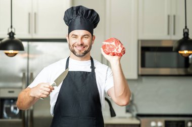 Erkek şef et tutar. Modern mutfakta et ve sığır eti hazırlayan bir adam. Milenyum adamı evdeki mutfakta çiğ et tutuyor. Çatallı dana fileto, kızarmış biftek. Biftek için çiğ et.