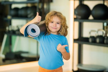 Spor salonunda yoga minderi tutan zinde bir çocuk. Yoga çocuk konsepti. Güçlü atletik fitness çocuğu. Çocuk Spor Konsepti