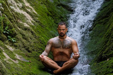 İnsan meditasyonu. Spor mankeni doğada rahatlar. Meditasyon, ruhsal sağlık. Sakin bir meditasyon adamı farkındalığı eğitiyor. Rahatlayın ve doğada meditasyon yapın. Sakin ol ve doğada rahatla.