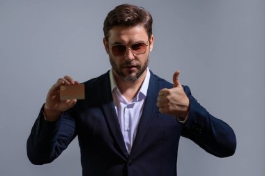 Gri arka planda kredi kartı tutan bir iş adamı. İspanyol adam kredi kartını gösteriyor. Kredi kartı ya da banka kartı. İnternetten alışveriş konsepti. İndirim teklifi, online alışveriş.