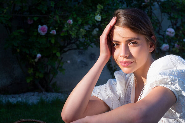 Сексуальная девушка возле цветка розы в весеннем парке. Молодая женщина в цветущем саду с розами. Модель красоты с весенними цветами. Счастливой весны. Красивая женщина наслаждается запахом цветов в весеннем парке