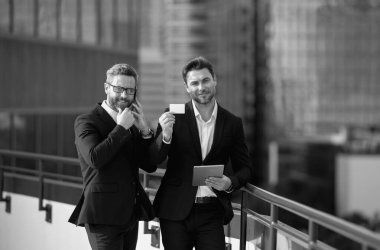 Tabletle ödeme yaparken kredi kartı tutan işadamları. Takım elbiseli iki iş adamı dışarıda kredi kartı ve laptop tableti tutuyor. Hesabı öde. Şehirde kredi kartı olan bir adam. İş anlaşması