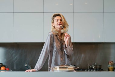 Ot pişiren, ev işi yapan bir kadın. Oda servisi konsepti. Mutfakta yemek hazırlayan seksi kadın. Ev mutfağında seksi pijama giyen bir kadın kahvaltı hazırlıyor.