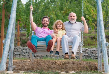 Men family playing on swing together Excited grandfather, amazed father and funny son swinging together in park outdoors. Fathers day concept. Generation concept clipart