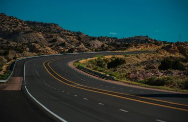 Mavi gökyüzünün altında asfalt otoyol ve tepe manzarası. Amerika 'da Yol