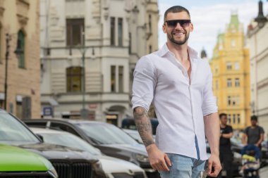 Yakışıklı adamın portresi. Hippi adam dışarıda modellik yapıyor. Şehirde güneş gözlüklü genç bir moda adamı. Kendine güvenen erkek model. Adam gururlu görünüyor. Avrupa caddesinde çekici bir adam. Zarif adam.