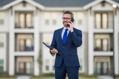 Emlakçı, takım elbiseli iş adamı. Elinde not defteri var ve telefonda konuşuyor. İş adamı. İş adamı komisyoncusu ya da emlakçı. Takım elbiseli bir iş adamı. Emlakçı.